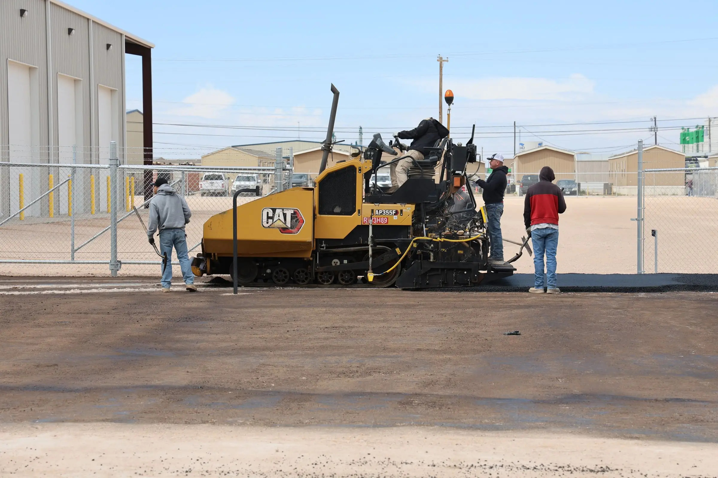 Asphalt paver laying a new surface with crew members raking the edge