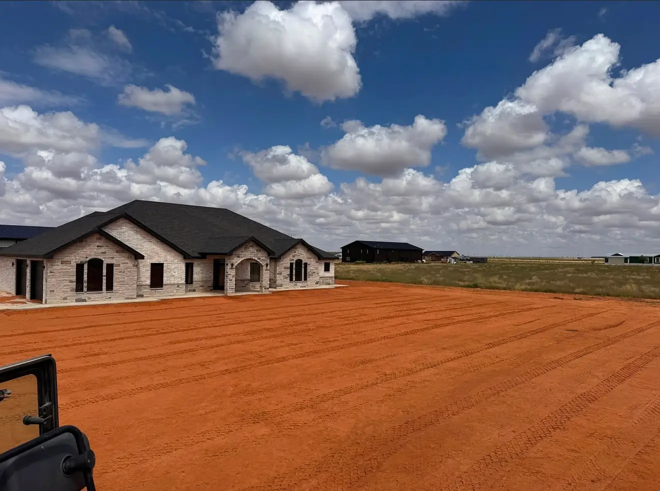 Graded red-dirt site beside a brick house under construction